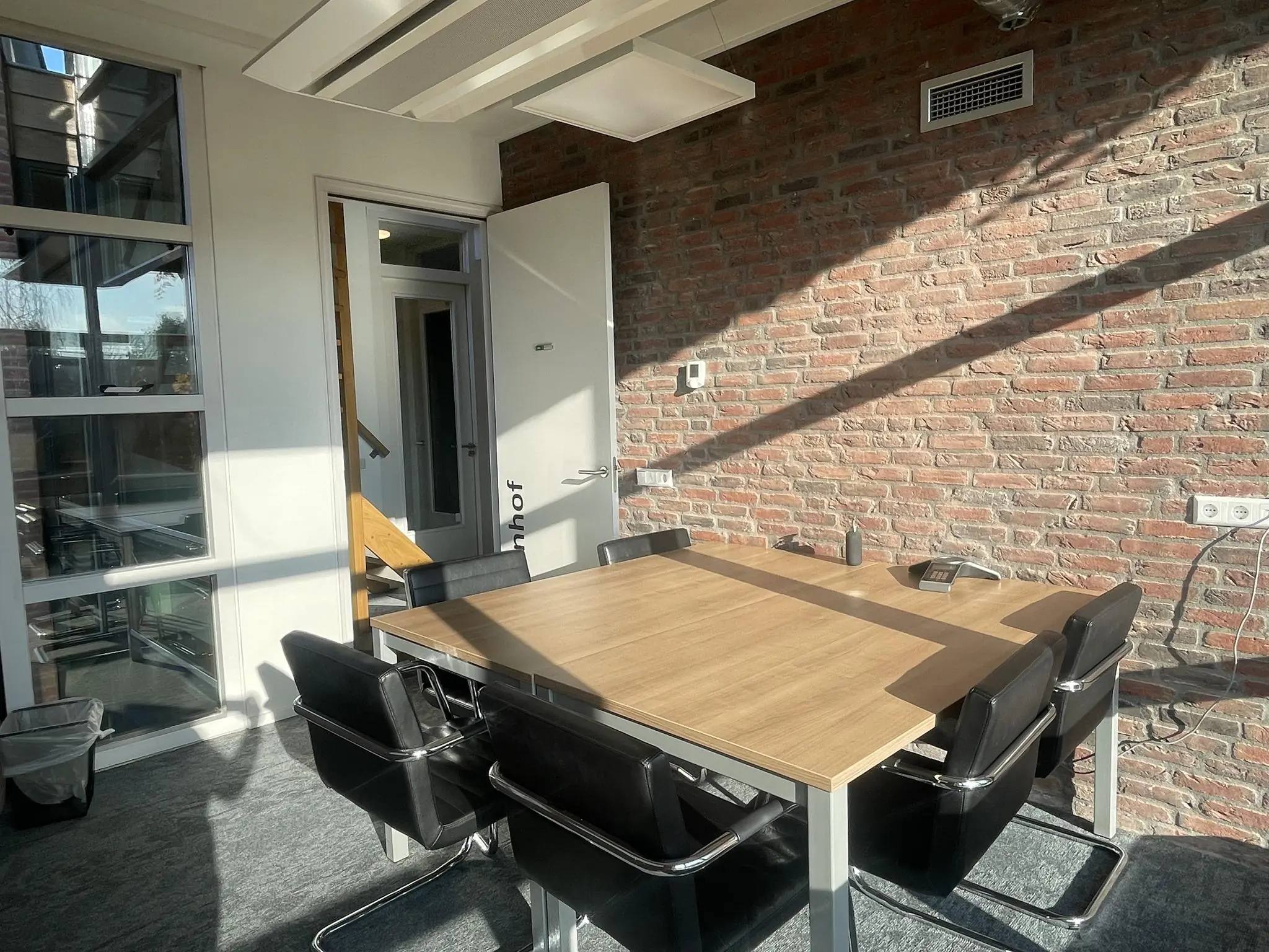 Vergaderruimte aan de Jan Leentvaarlaan met een houten tafel, zes zwarte stoelen en een bakstenen muur.